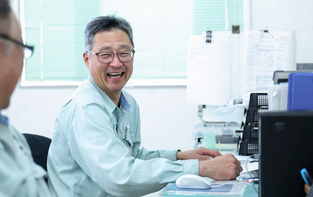 隣のデスクの同僚と笑顔で会話するY.Kさん